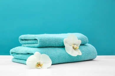 Stack of soft clean towels with beautiful flowers on table against color background. Space for text