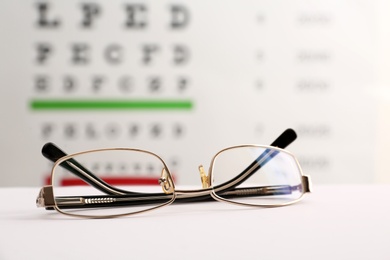 Photo of Glasses with corrective lenses on table against eye chart
