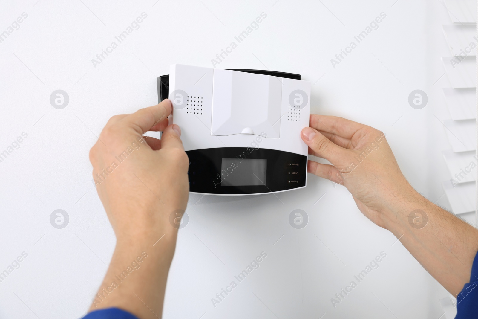 Photo of Man installing home security alarm system on white wall indoors, closeup