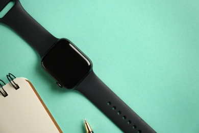 Photo of Stylish smart watch and notebook on turquoise background, flat lay. Space for text