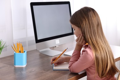 Photo of E-learning. Girl taking notes during online lesson at table indoors