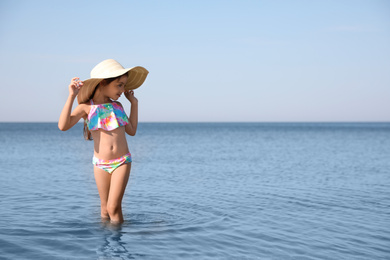 Cute little child with straw hat in sea on sunny day. Beach holiday