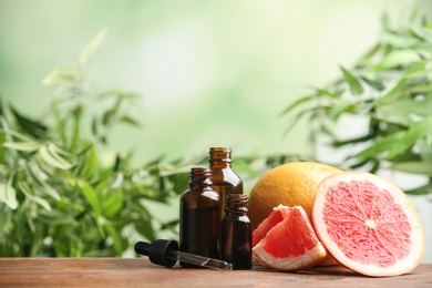 Bottles of essential oil and grapefruit slices on table against blurred background. Space for text