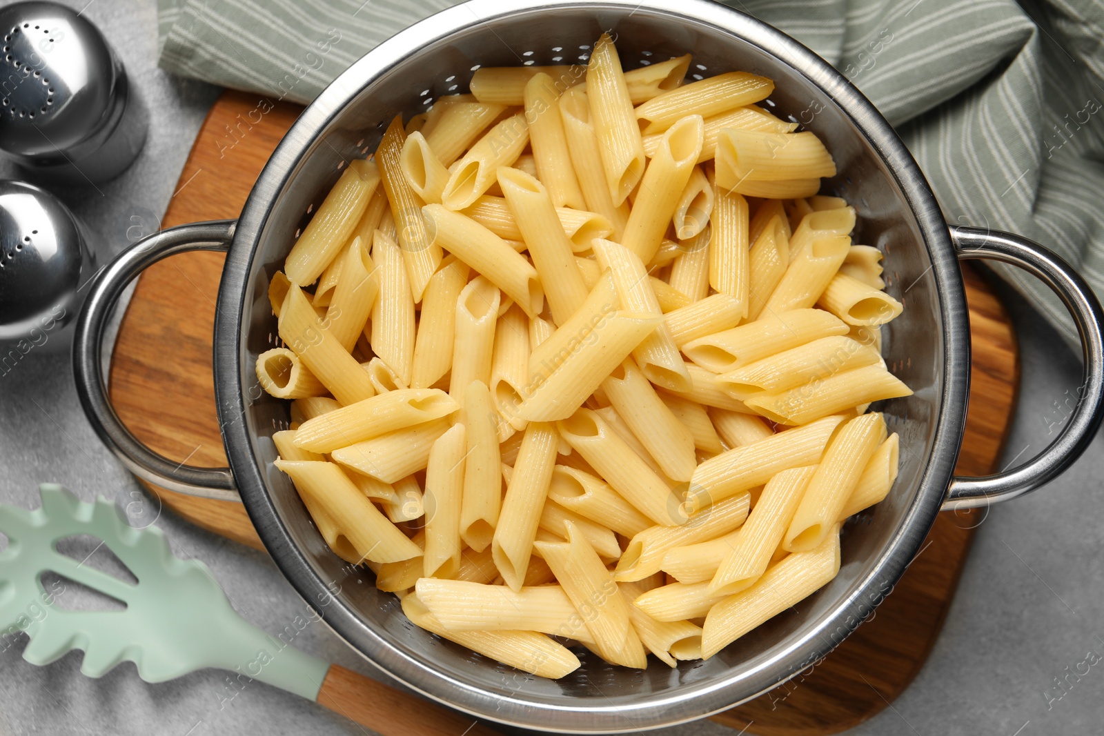 Photo of Delicious penne pasta in colander, spices and spoon on gray table, flat lay