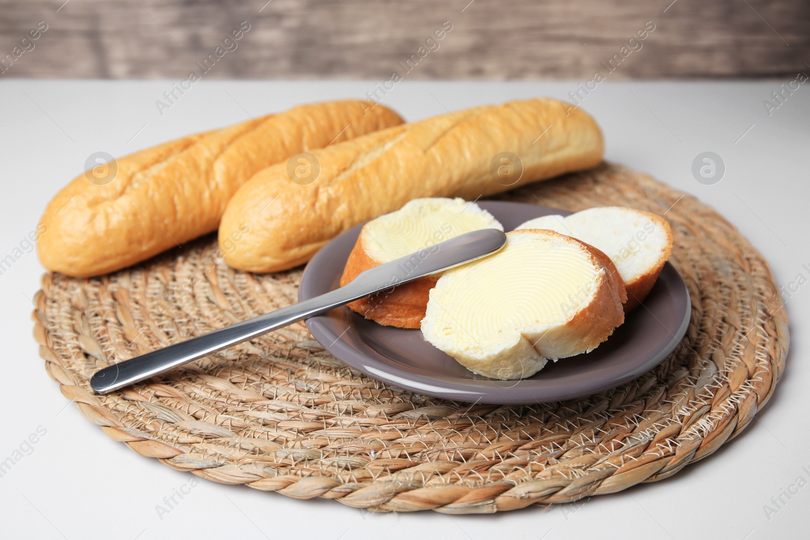 Photo of Whole and cut baguettes with fresh butter on white table