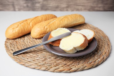 Photo of Whole and cut baguettes with fresh butter on white table