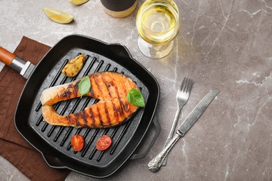 Frying pan with tasty salmon steak and wine on grey background