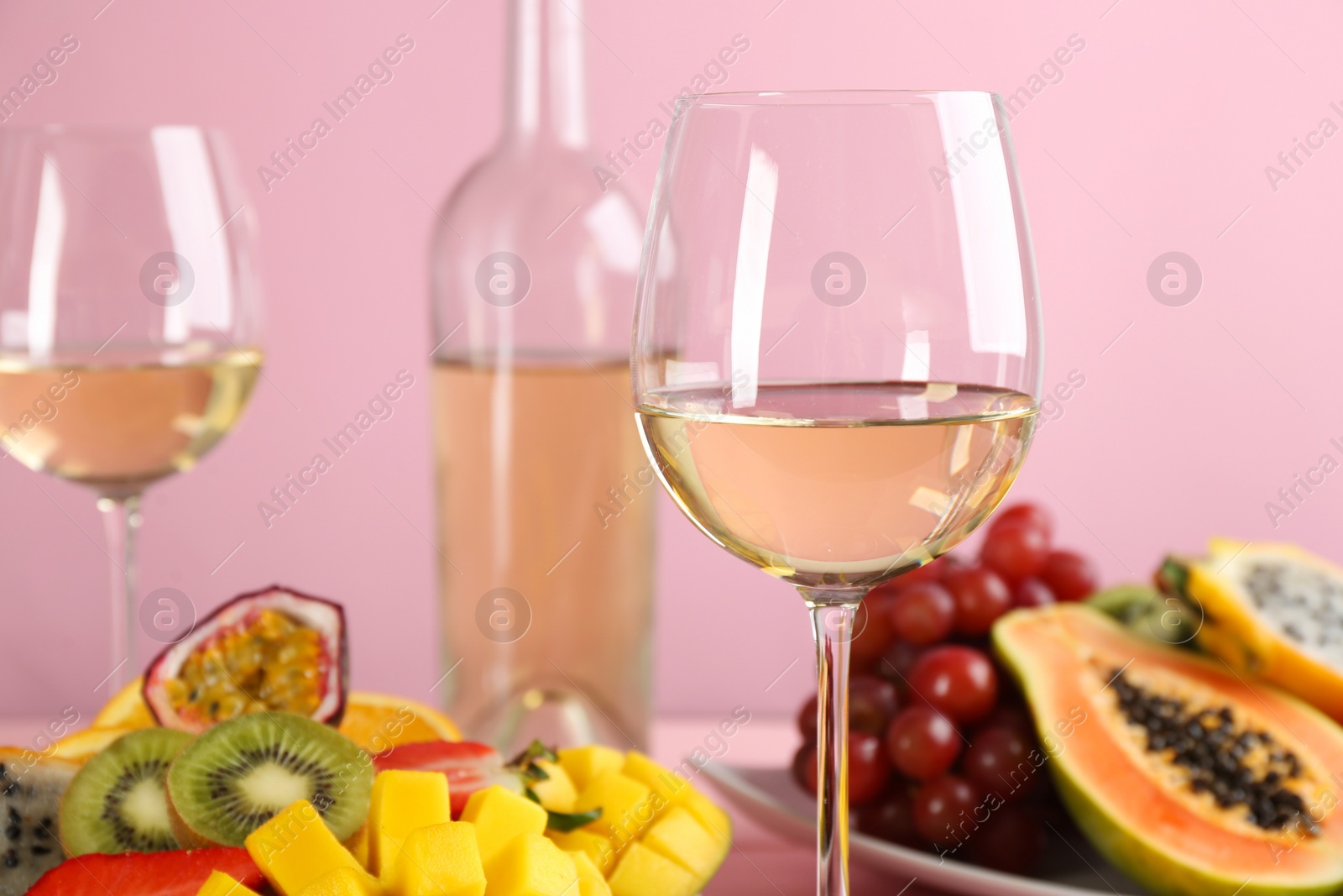 Photo of Delicious exotic fruits and glasses of wine on pink background, closeup