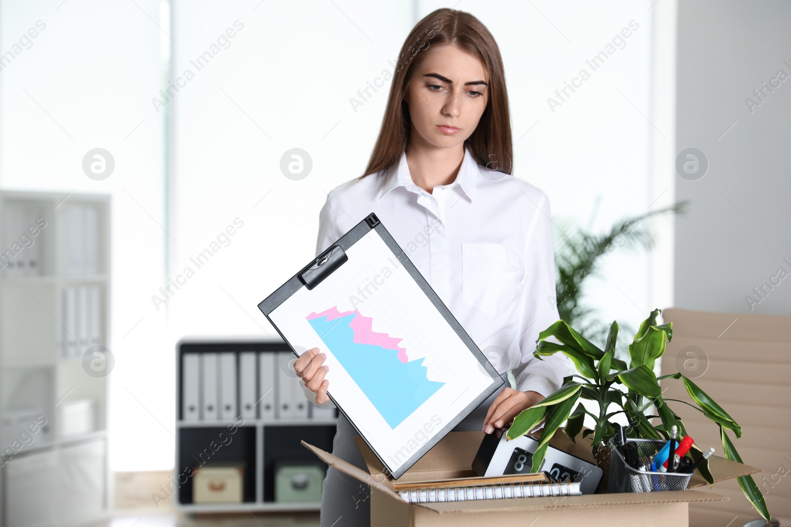 Photo of Upset young woman packing stuff in box at office