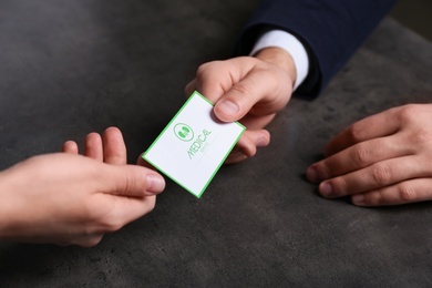 Man giving medical business card to woman on dark background, closeup. Nephrology service