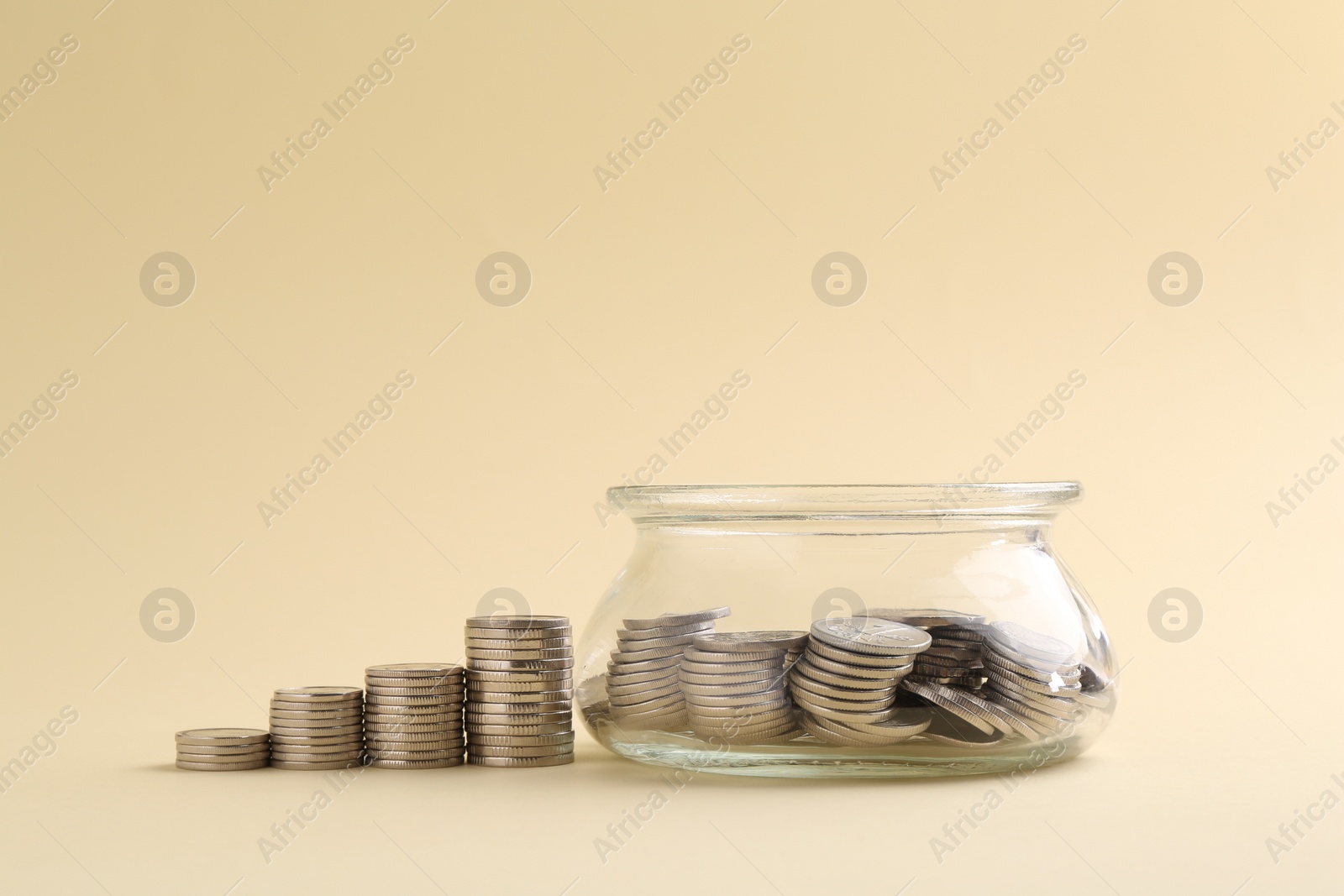 Photo of Financial savings. Coins and glass jar on beige background