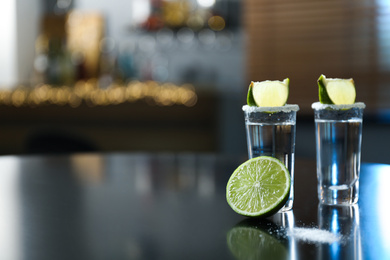 Photo of Mexican Tequila with salt and lime slices on black table at bar. Space for text