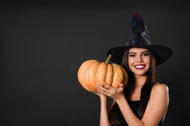 Photo of Beautiful woman wearing witch costume with pumpkin for Halloween party on black background, space for text