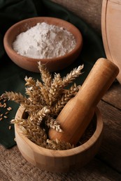 Photo of Mortar with spikes and bowl of wheat flour on wooden table