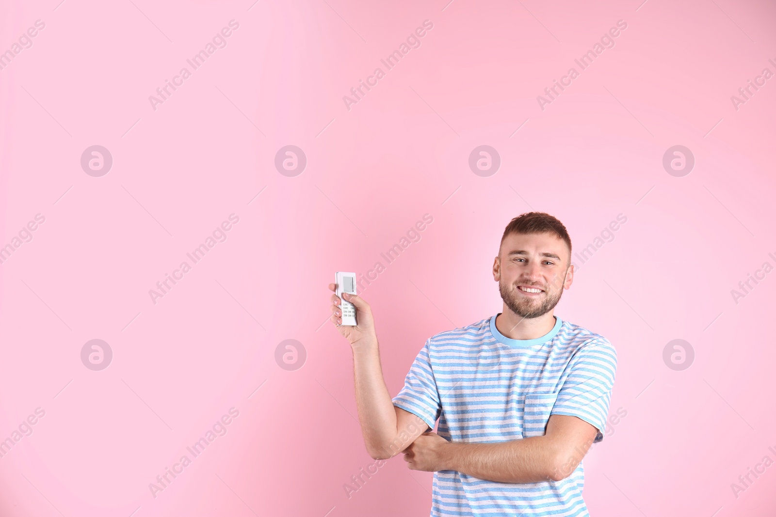 Photo of Young man with air conditioner remote on color background, copy space text