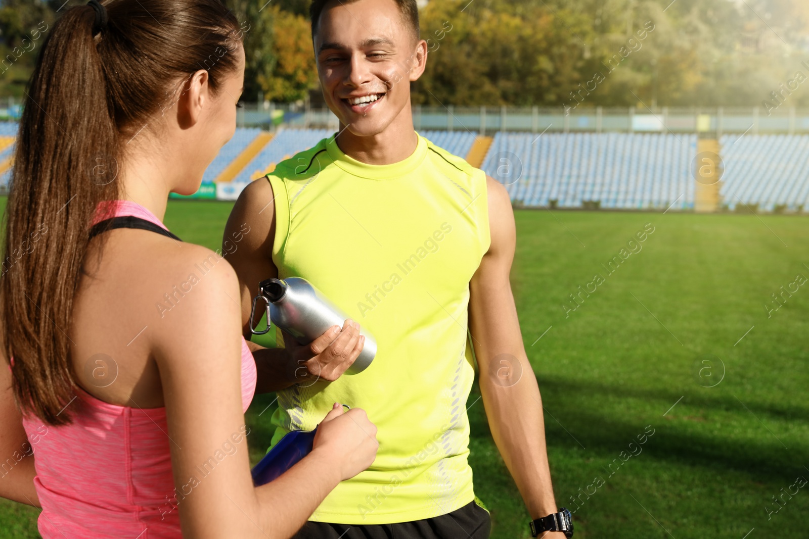 Photo of Young sporty couple holding bottles of water at stadium on sunny day