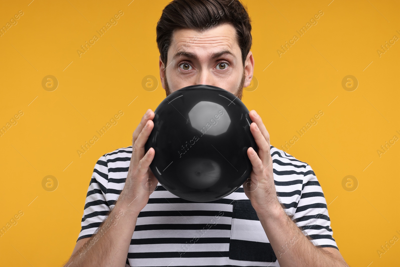 Photo of Man inflating black balloon on yellow background
