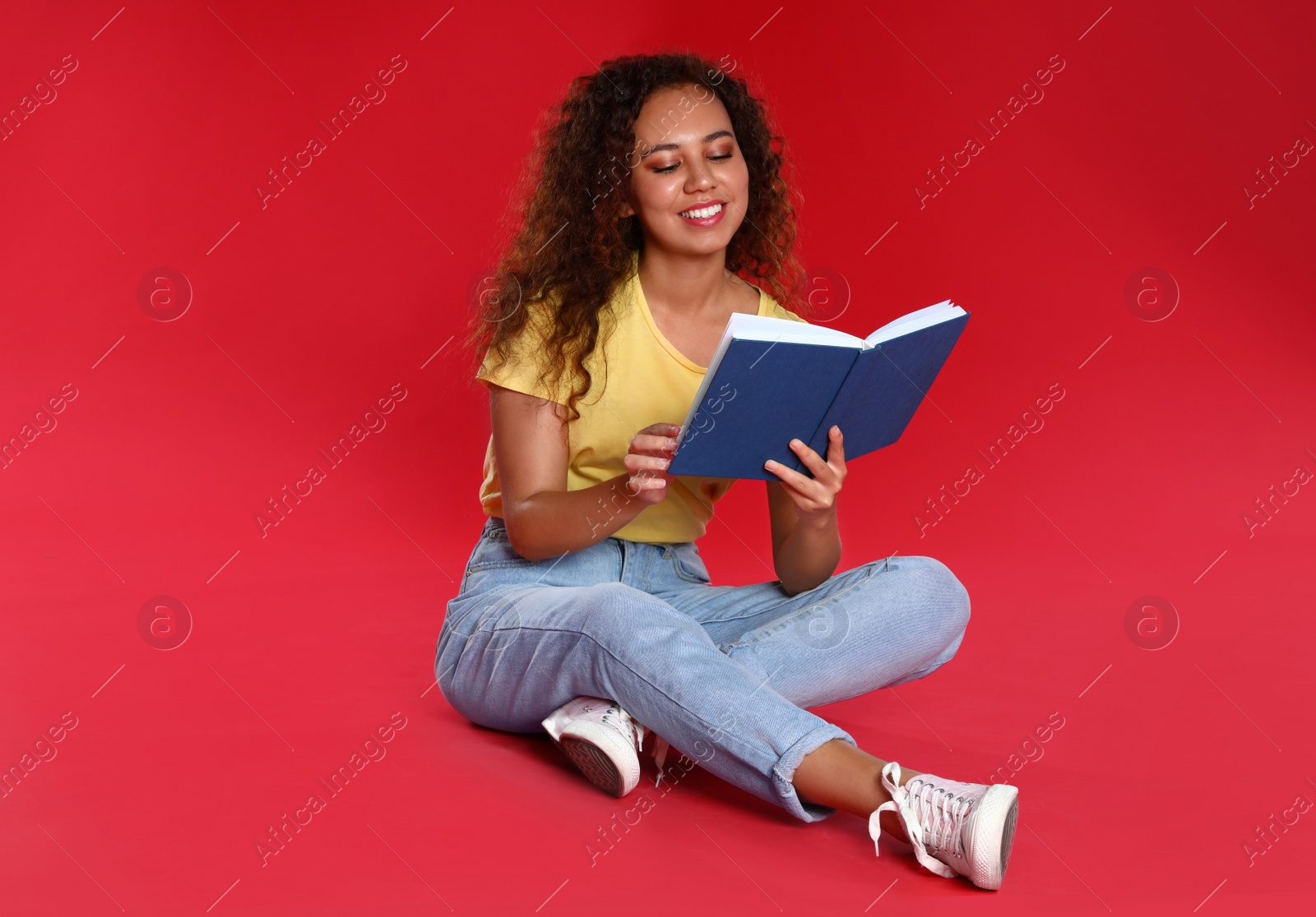 Photo of Beautiful African-American young woman reading book on red background