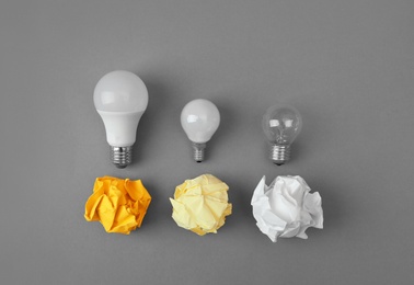 Photo of Flat lay composition with lamp bulbs and crumpled paper on grey background