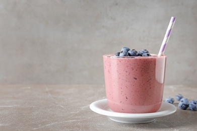 Glass with blueberry smoothie on grey table. Space for text