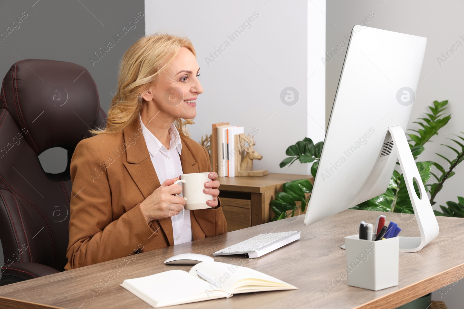 Photo of Lady boss with cup of drink near computer at desk in office. Successful businesswoman