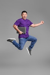 Emotional man with laptop jumping on grey background