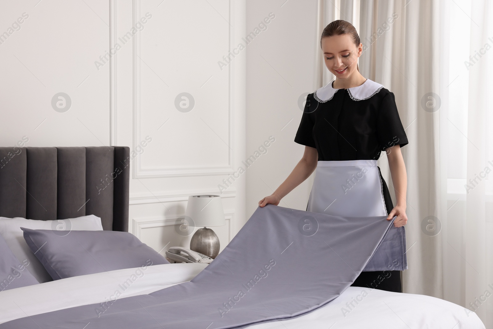 Photo of Young maid making bed in hotel room. Space for text