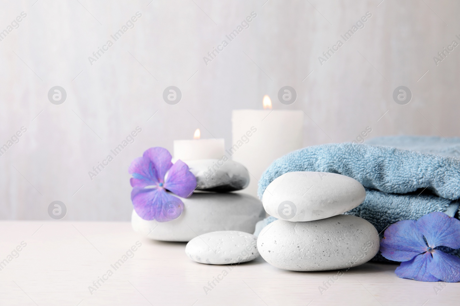 Photo of Composition with zen stones, towel and candles on table against light background. Space for text