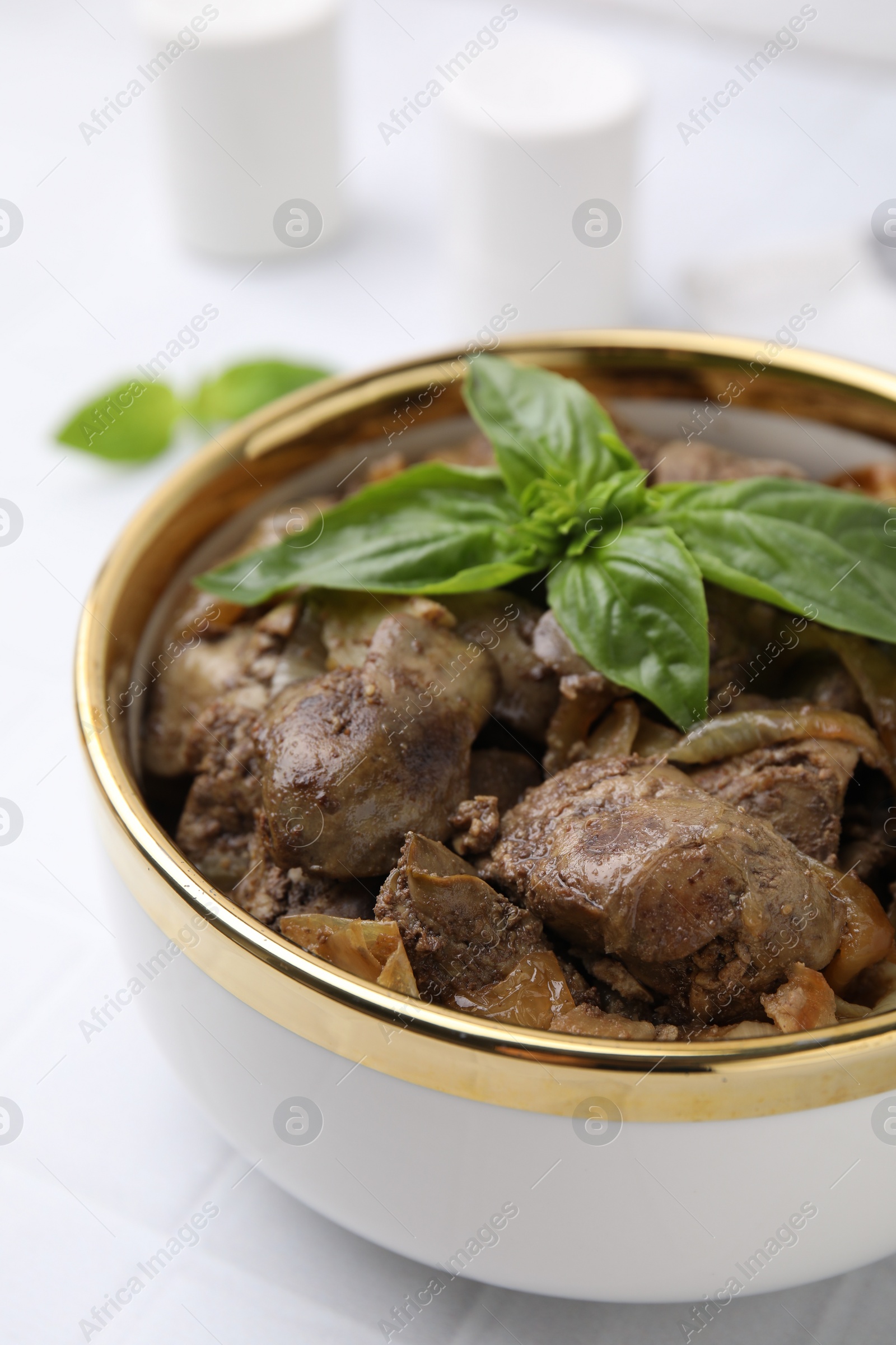 Photo of Delicious fried chicken liver with onion and basil in bowl on white table, closeup