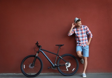 Photo of Handsome man with modern bicycle near red wall outdoors