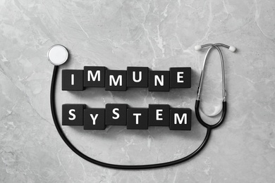 Photo of Cubes with words Immune System and stethoscope on light grey table, flat lay