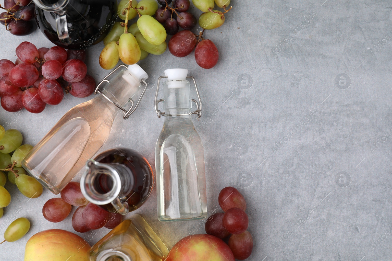 Photo of Different types of vinegar and fresh fruits on grey table, flat lay. Space for text