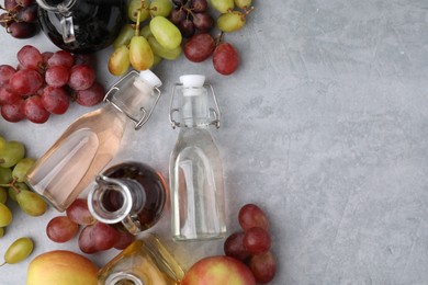 Different types of vinegar and fresh fruits on grey table, flat lay. Space for text