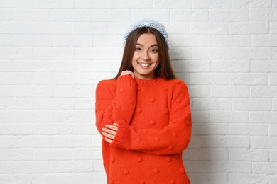 Beautiful young woman in warm sweater with hat near white brick wall