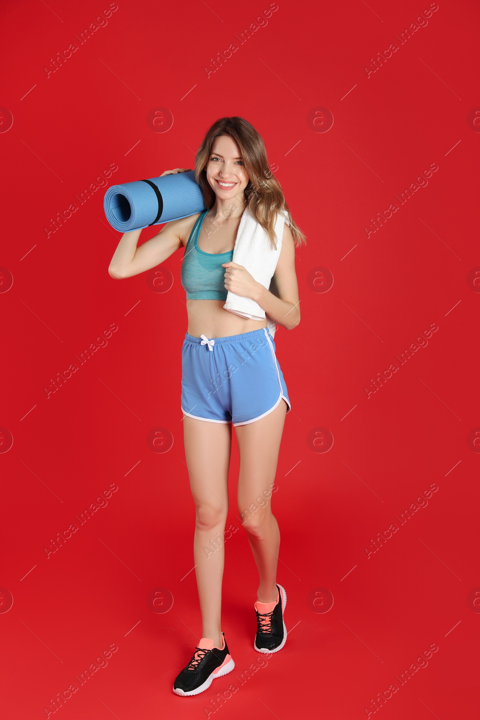 Photo of Beautiful woman with yoga mat and towel on red background
