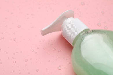 Photo of Wet bottle of face cleansing product on pink background, closeup. Space for text