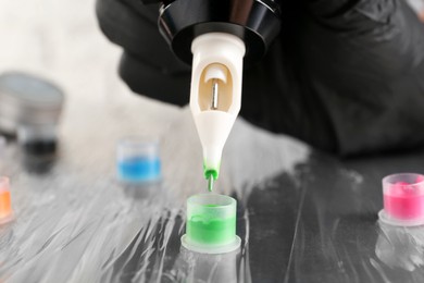 Photo of Tattoo artist with professional machine and colorful inks at table, closeup