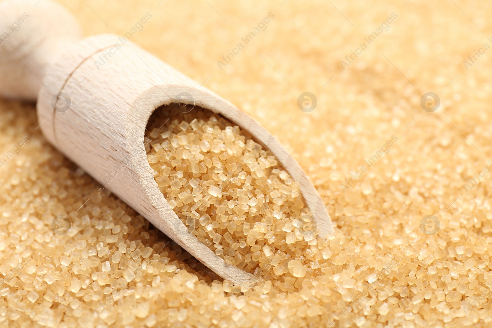 Photo of Wooden scoop on granulated brown sugar, closeup view