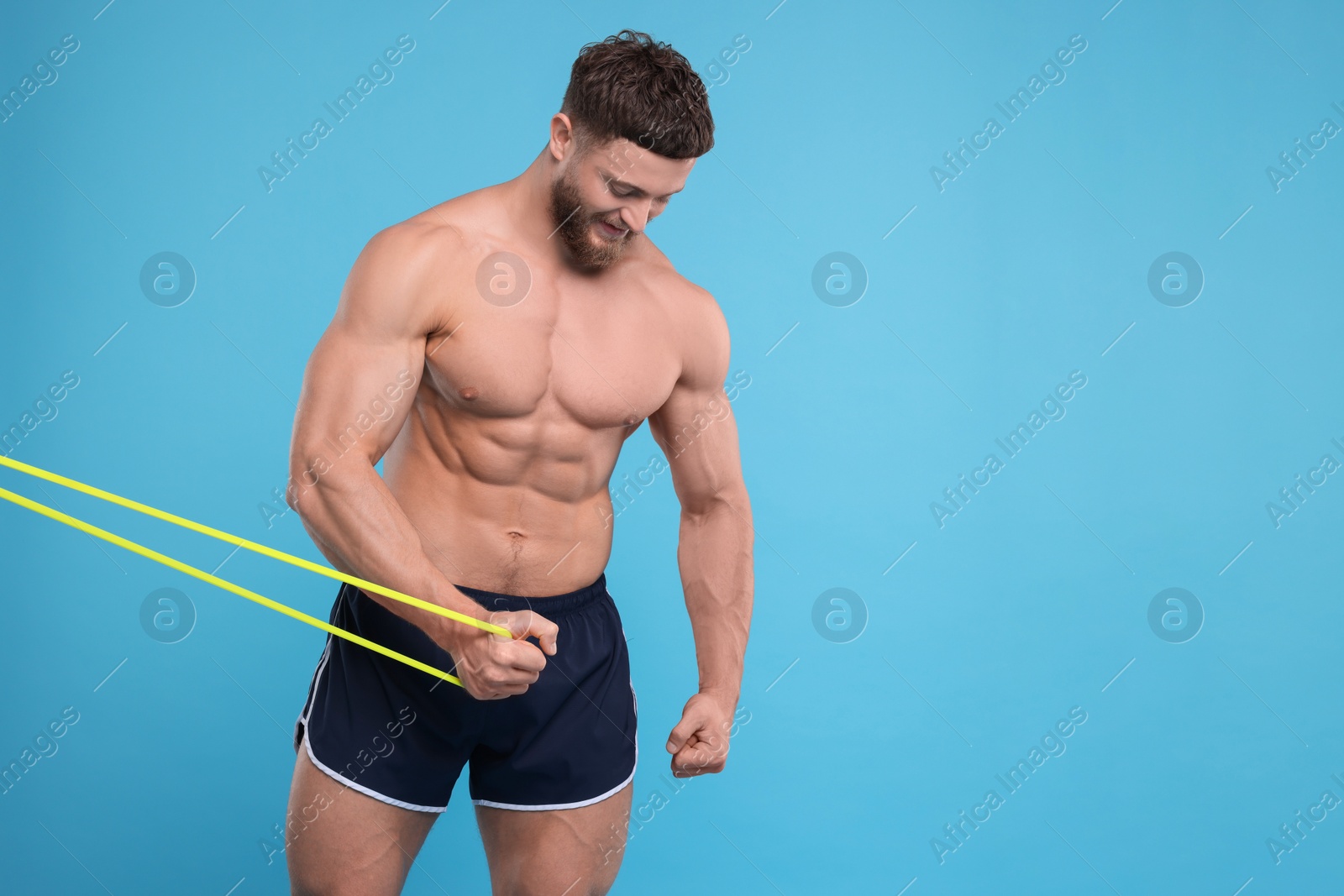 Photo of Young man exercising with elastic resistance band on light blue background. Space for text