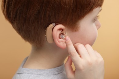 Photo of Little boy with hearing aid on pale brown background, closeup
