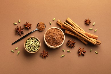Photo of Cinnamon sticks, powder, star anise and cardamom pods on brown background, flat lay