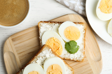 Tasty egg sandwiches served with coffee on white wooden table, flat lay