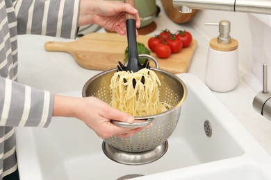 Woman with colander of cooked spaghetti and pasta server at sink, closeup
