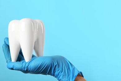 Dentist holding ceramic model of tooth on color background, space for text