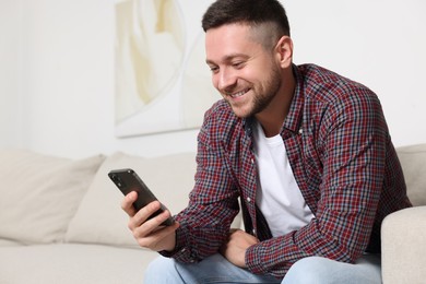 Photo of Handsome man sending message via smartphone on sofa at home