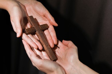 Easter - celebration of Jesus resurrection. Women holding wooden cross on dark background, closeup