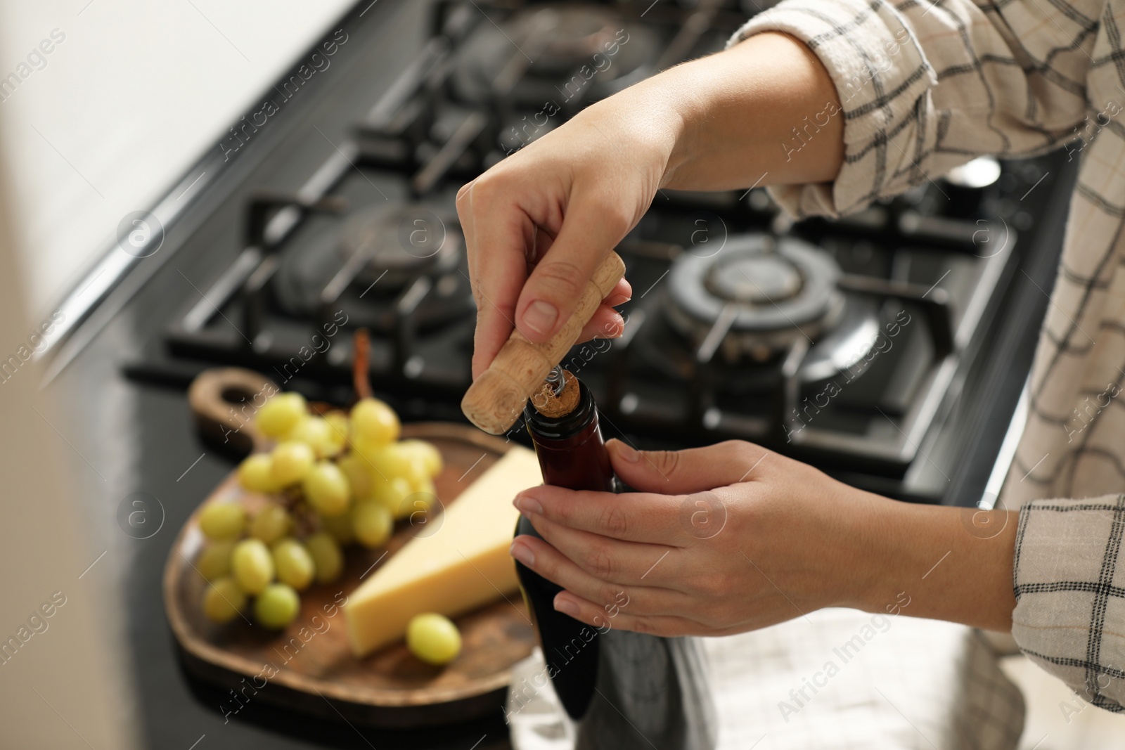 Photo of Woman opening wine bottle with corkscrew at countertop indoors, closeup