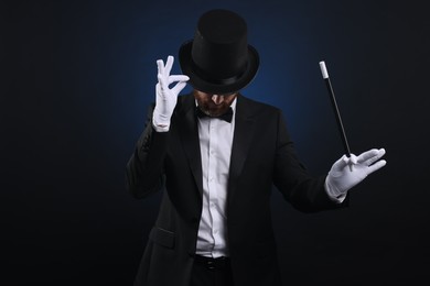 Photo of Magician in top hat holding wand on dark blue background