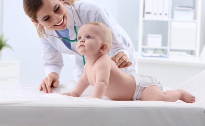 Photo of Children's doctor examining baby with stethoscope in hospital. Space for text