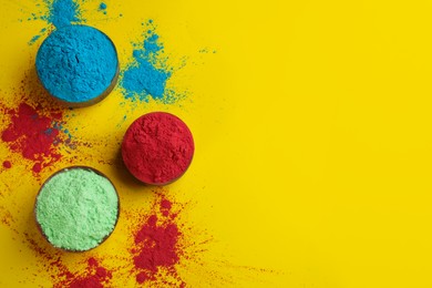 Photo of Colorful powders in bowls on yellow background, flat lay with space for text. Holi festival celebration